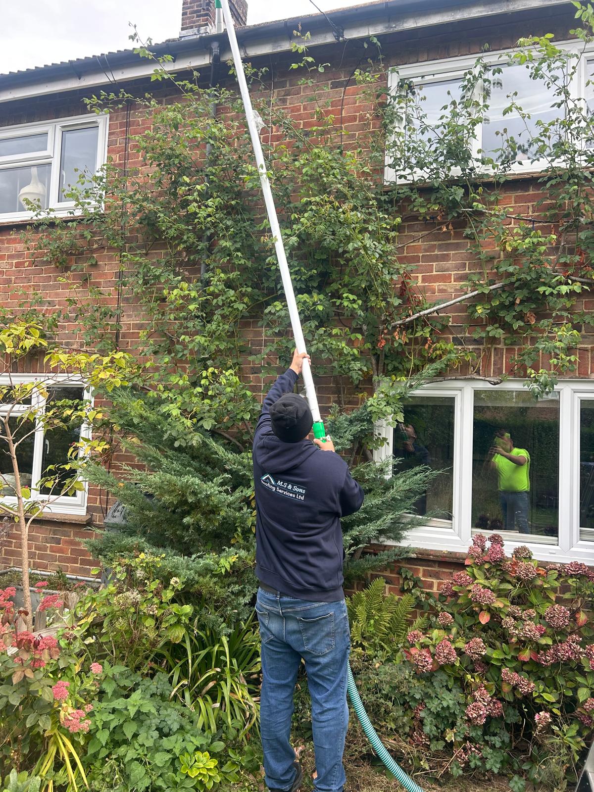 Technician cleaning gutters at a brick home